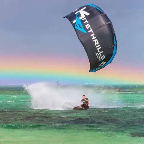 Kitesurfeur sous une aile Kitethrills, sillage d'écume et arc-en-ciel