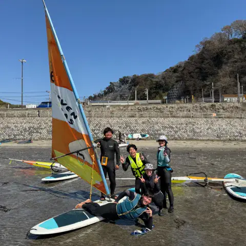 Groupe d'élèves avec leurs planches et une voile sur la plage