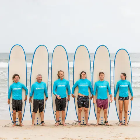 Groupe d'élèves alignés avec leurs planches sur la plage