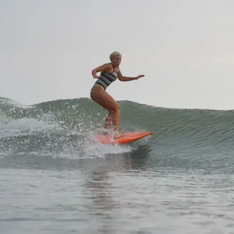 Surfeuse debout sur sa planche dans une vague