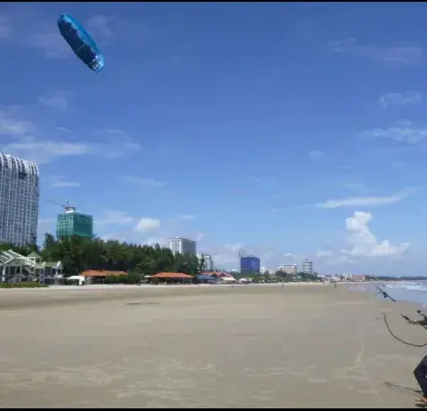 Pilote d'aile sur la plage de sable, immeubles derrière