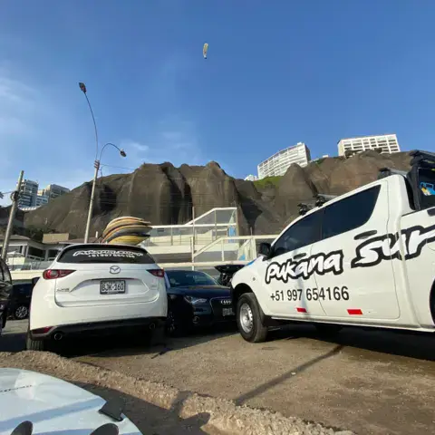 Pick-up de l'école Pukana Surf garé au pied de la falaise