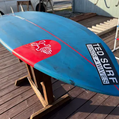 Planche de surf TED SURF présentée sur la terrasse en bois