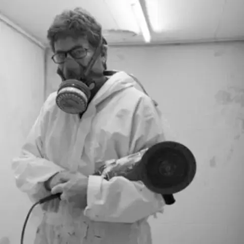 Artisan masqué avec une ponceuse dans la salle de finition