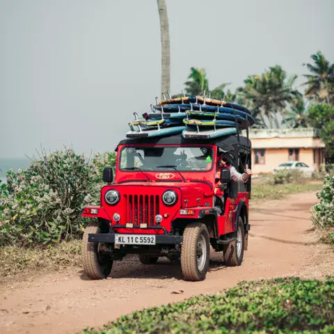 Une jeep rouge chargée de planches sur un chemin du village