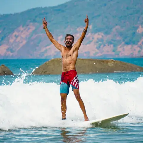 Un surfeur lève les bras sur une vague