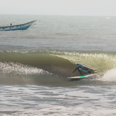 Un surfeur dans le tube d'une vague, un bateau de pêche au loin