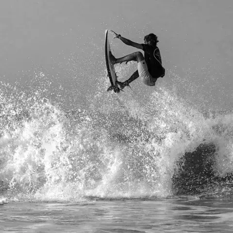Un surfeur en l'air au-dessus d'une vague (noir et blanc)