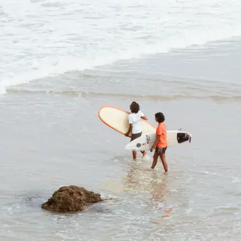 Un moniteur et un élève avec leurs planches entrent dans l'eau