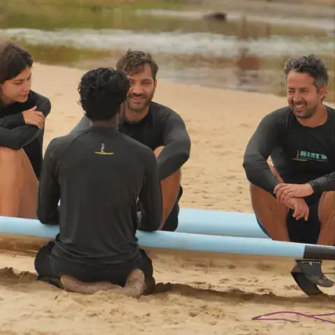 Élèves assis sur la plage avec leurs planches avant le cours