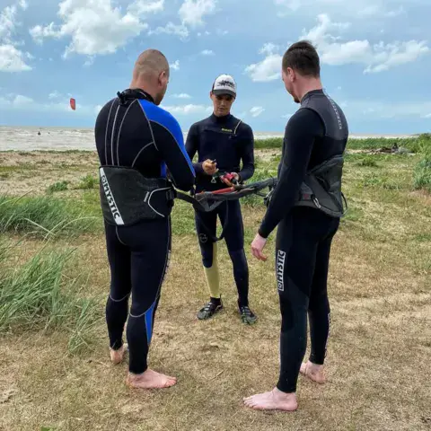 Trois kitesurfeurs en combinaison sur la dune, avant de partir à l'eau