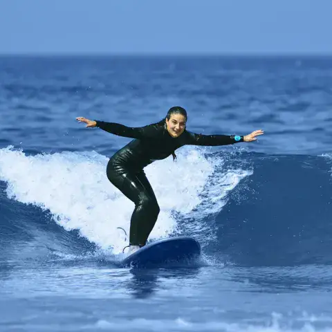 Surfeuse debout sur sa planche dans une vague