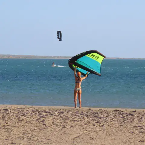 Rider avec une aile de wing sur la plage, kiters sur l'eau en arrière-plan