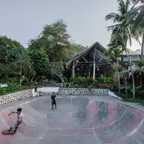 Le skate bowl du camp et un bâtiment en bois au milieu des palmiers