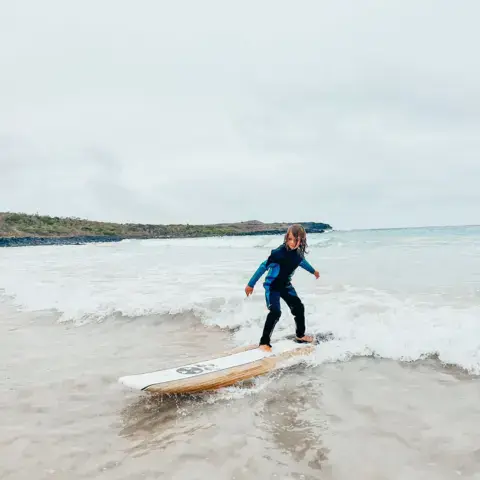 Élève debout sur sa planche dans les petites vagues