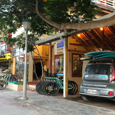 Devanture du magasin avec les vélos de location et les planches sur le toit d'un véhicule