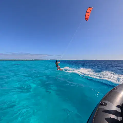 Kitesurfeur sur une eau turquoise, bateau de sécurité au premier plan