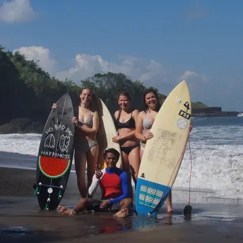 Groupe de surfeuses avec leurs planches sur une plage de sable noir