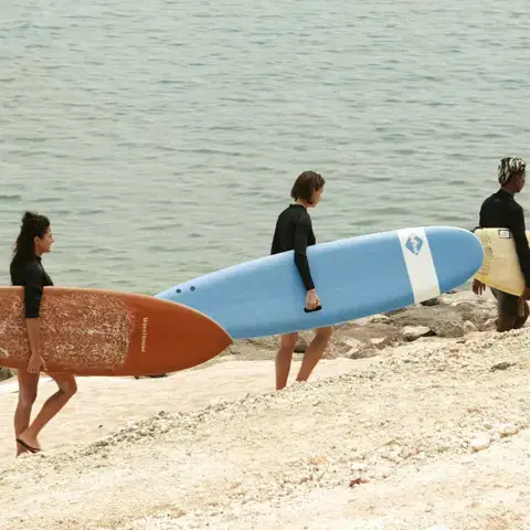 Trois surfeurs portant leurs planches au bord de l'eau