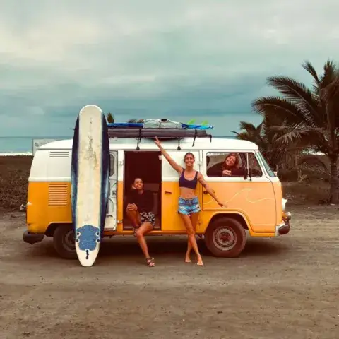 Combi jaune garé sur la plage, planche de surf contre le véhicule
