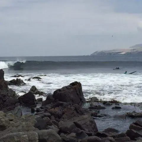 Vague déferlant sur la côte rocheuse, avec des surfeurs à l'eau