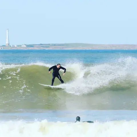 Surfeur sur une vague face au phare
