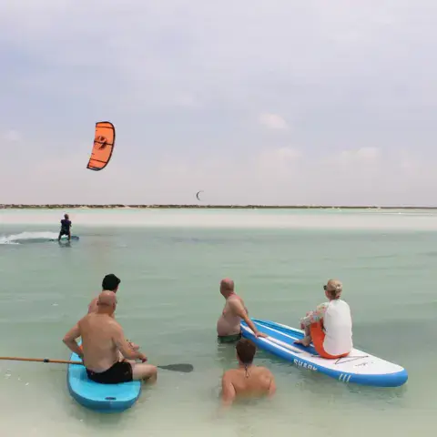 Élèves sur des paddles pendant un cours, un kitesurfeur au large