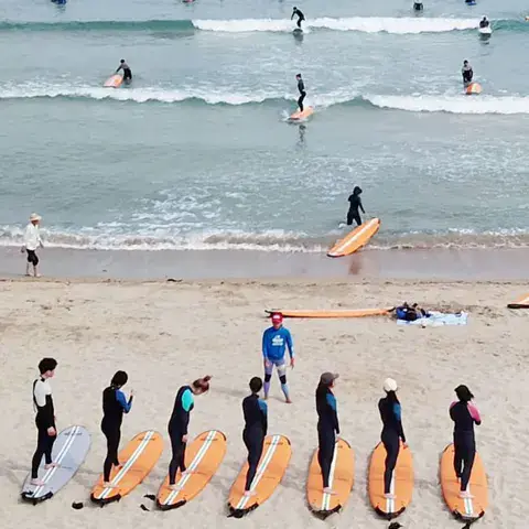 Groupe d'élèves alignés avec leurs planches sur la plage