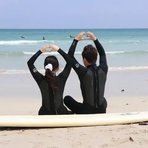 Deux élèves assis devant la mer, planche sur le sable