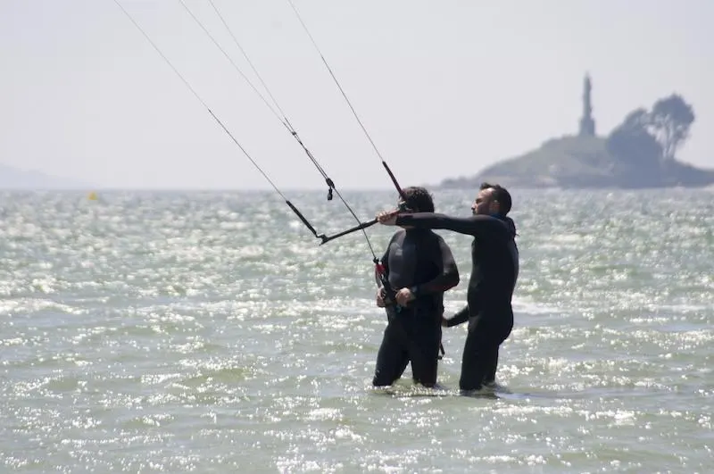 Cours de kitesurf dans l'eau peu profonde, un moniteur et un élève tenant la barre