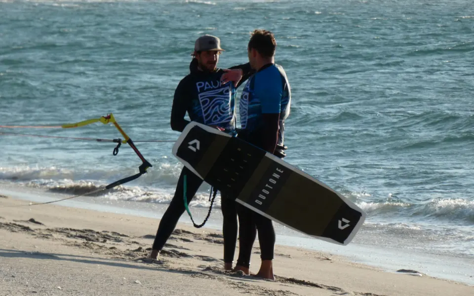 Deux personnes sur la plage avec une planche de kitesurf et une barre