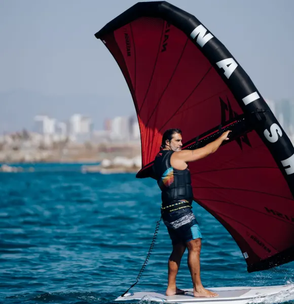 Pratiquant de wingfoil avec une aile rouge, la ville en arrière-plan