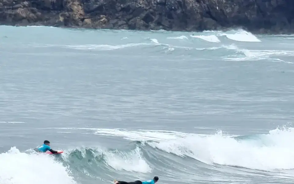 Élèves allongés sur leur planche dans les vagues devant un îlot rocheux