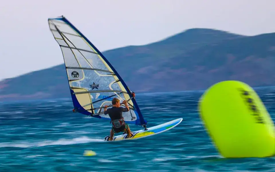 Windsurfeur passant près d'une bouée jaune, relief en arrière-plan