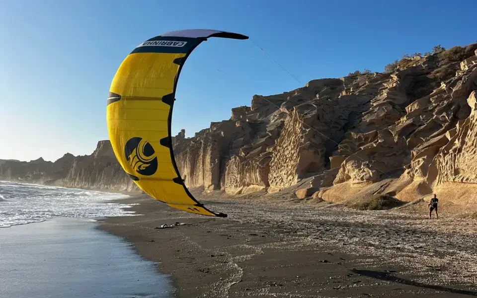 Aile de kite jaune devant une falaise et une plage de sable noir