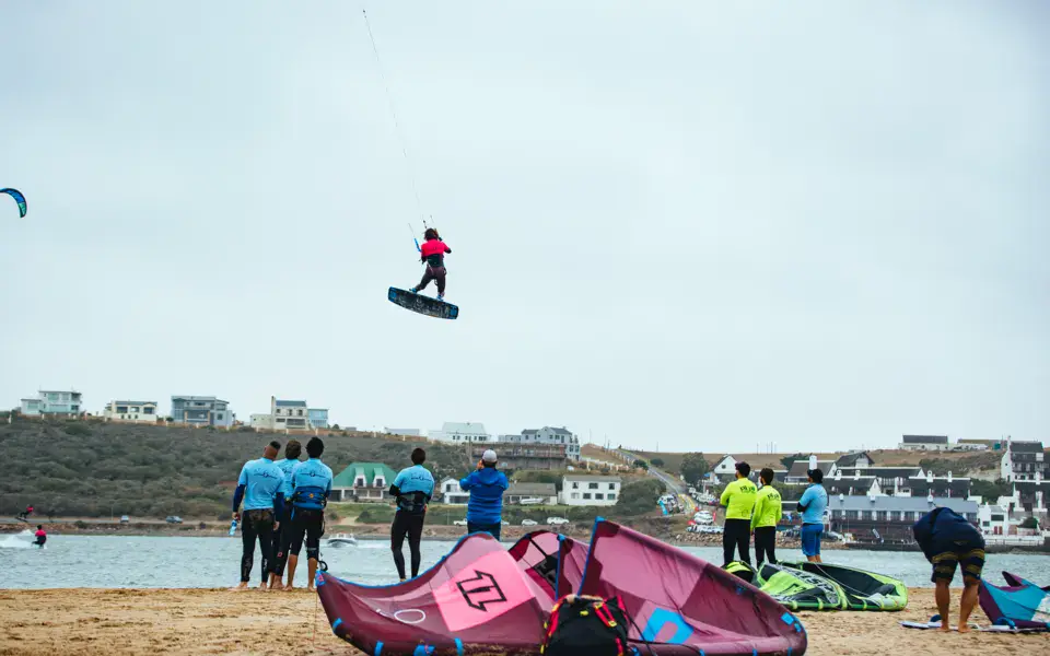 Kitesurfeur en saut au-dessus de l'eau, groupe et ailes sur la plage