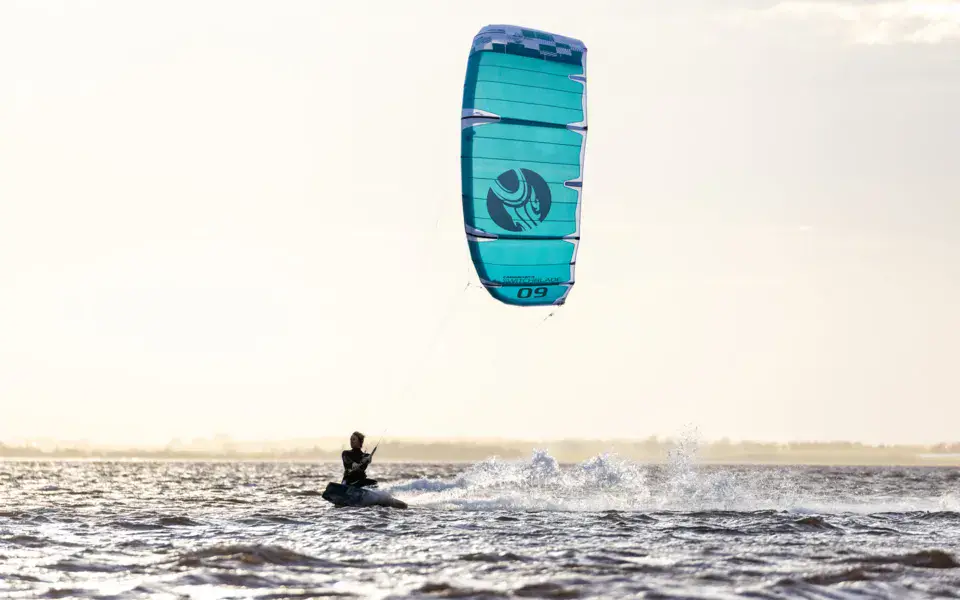 Kitesurfeur sous une aile bleue, sur l'eau plate