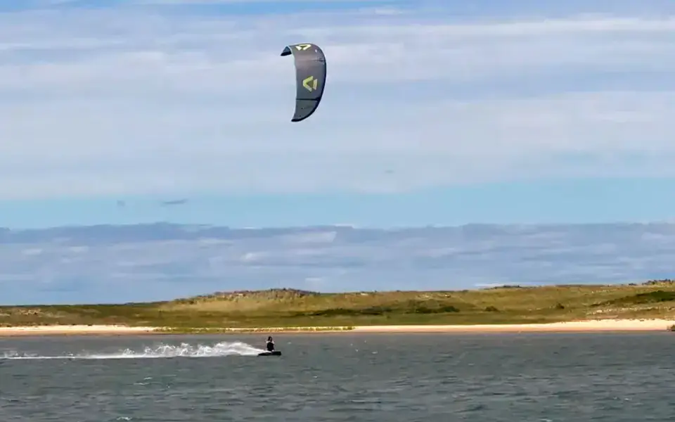 Kitesurfeur sur un plan d'eau calme, dunes en arrière-plan
