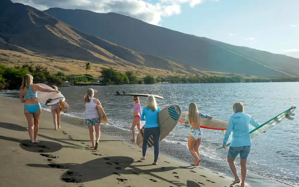 Groupe qui marche sur la plage avec ses planches, face aux montagnes