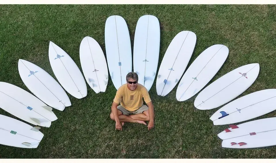 Le shaper assis au milieu d'un arc de planches blanches