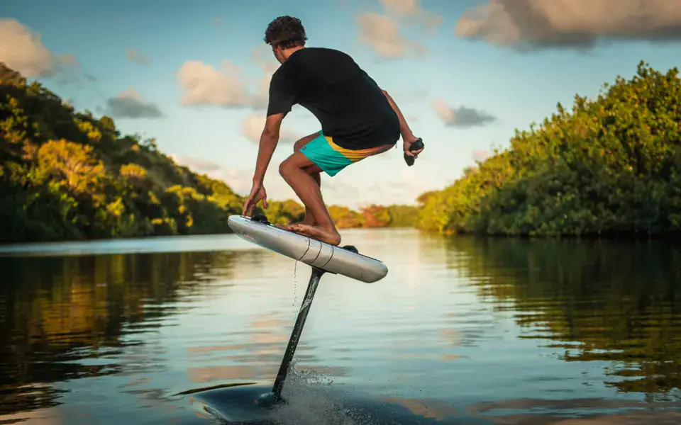 Rider sur un e-foil, au bord d'une rive boisée