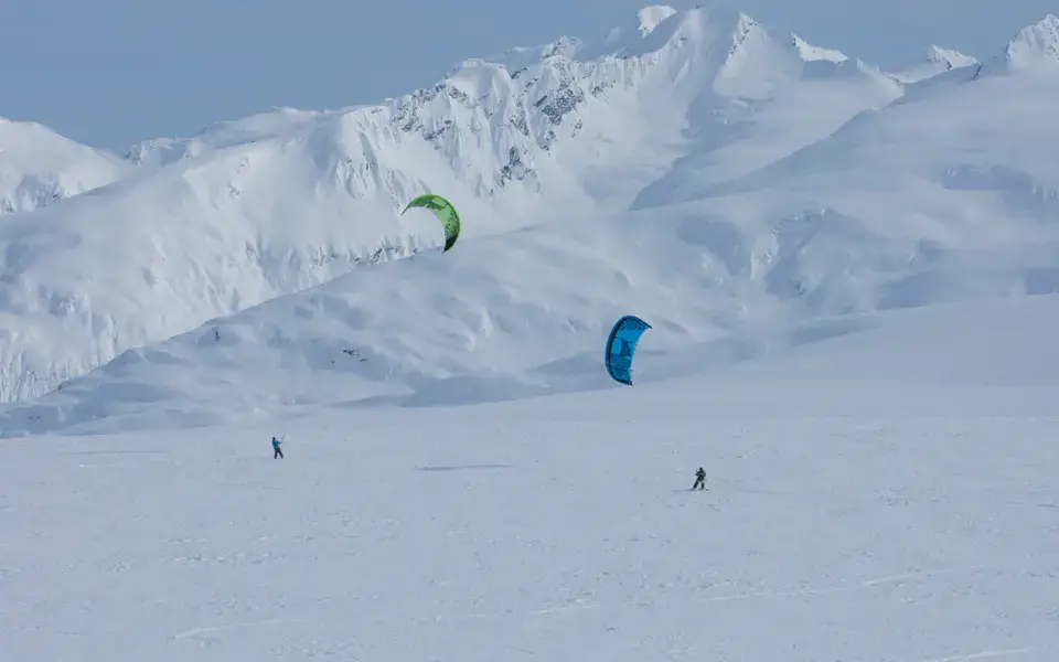 Deux snowkiteurs sur un grand plateau enneigé, montagnes en fond
