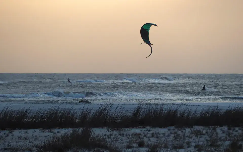 Kitesurfeur au coucher du soleil devant une plage bordée de dunes