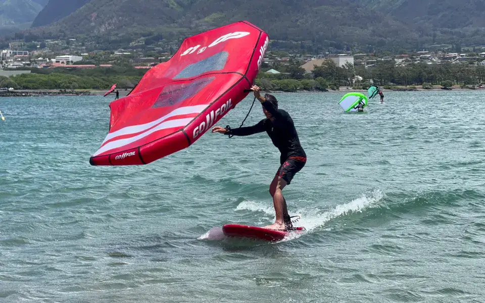 Rider de wing foil avec une aile rouge sur une eau peu profonde, montagnes à l'arrière-plan