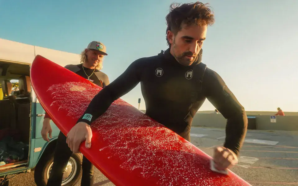 Un surfeur prépare sa planche à la cire devant le van de l'école