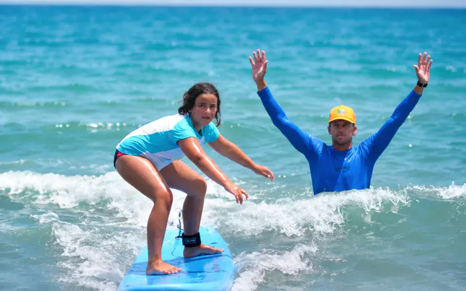 Un moniteur encourage une élève debout sur sa planche de surf pendant un cours
