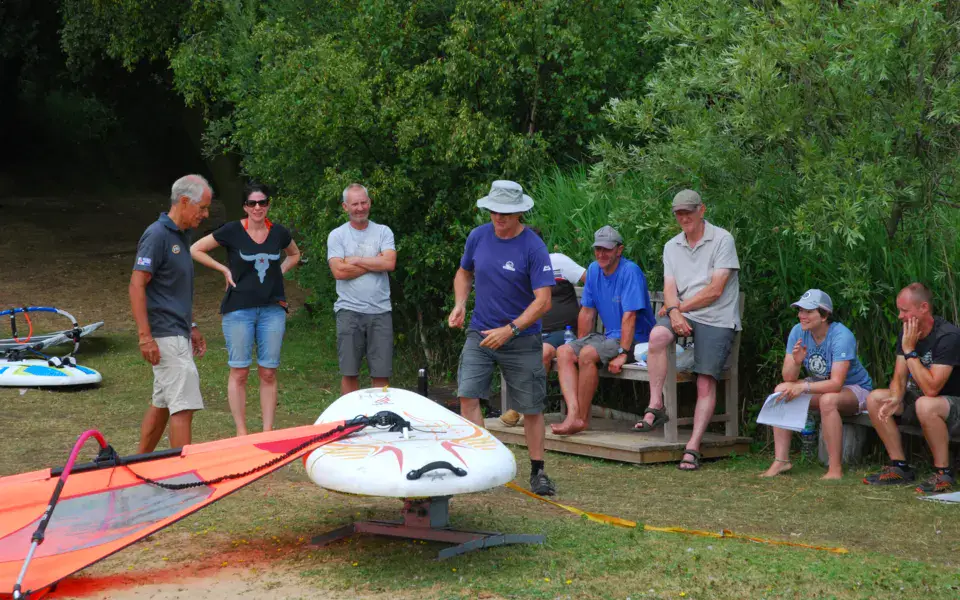 Membres du club au bord de l'eau, planche et voile au sol