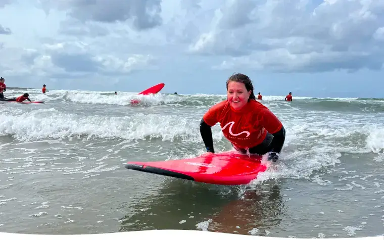 Élève à genoux sur sa planche rouge dans les vagues