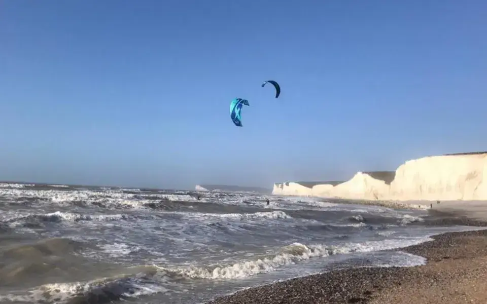 Kitesurfeur au large d'une plage de galets, falaises blanches au fond
