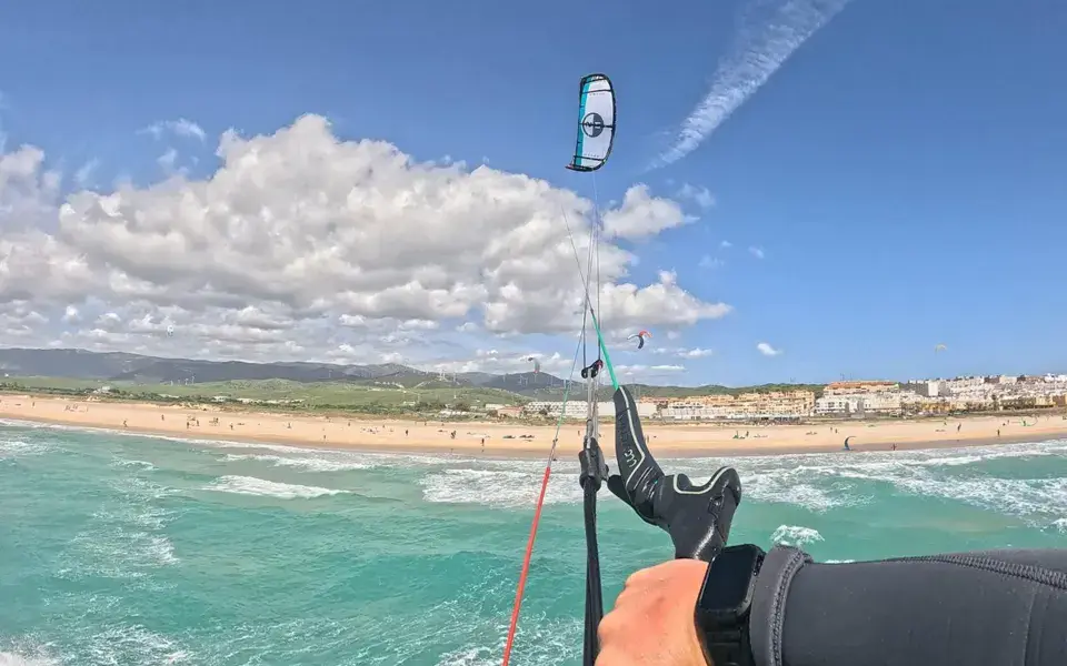 Vue à la première personne d'un kitesurfeur, barre en main, au-dessus de l'eau turquoise